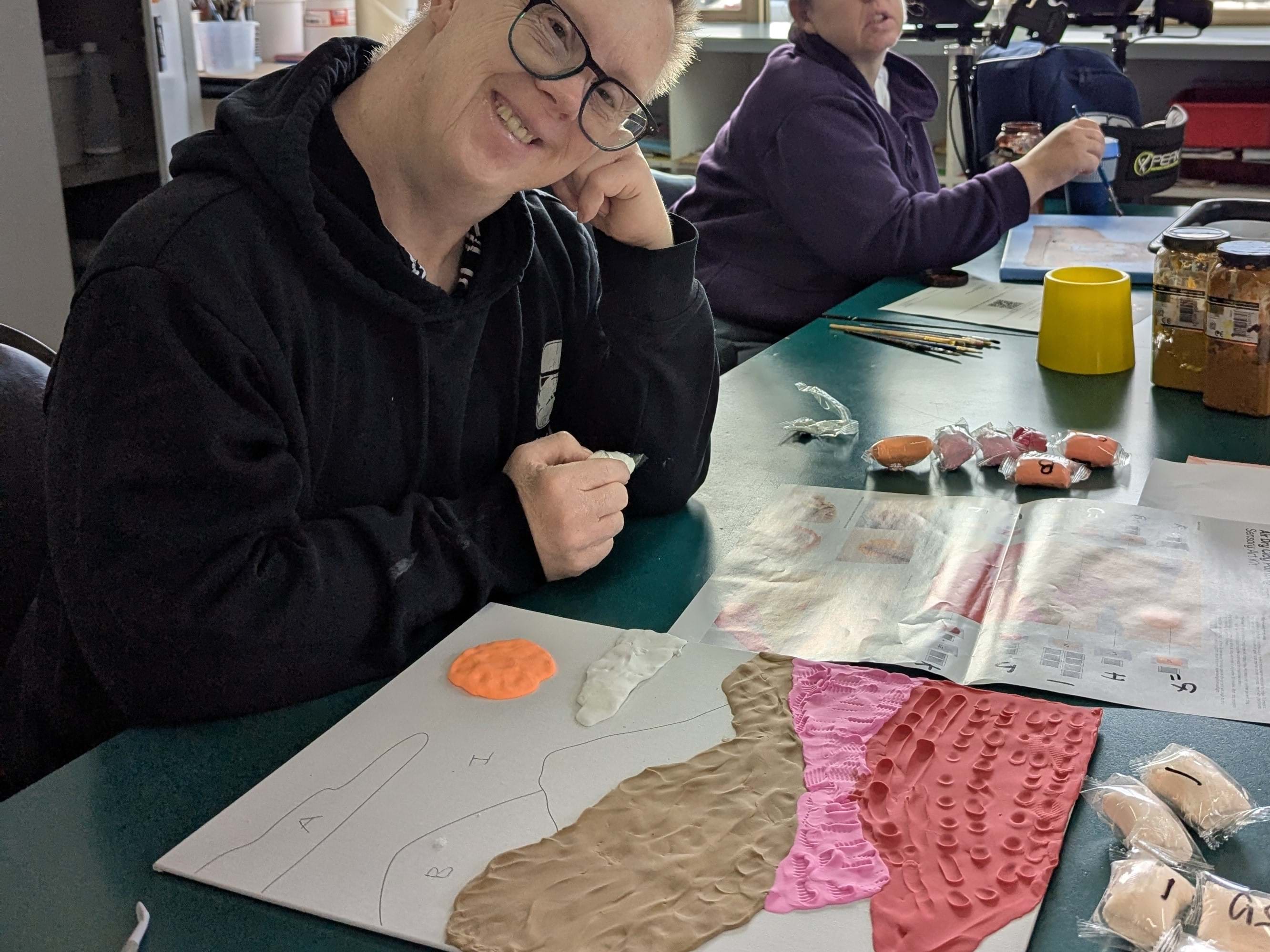 A man smiling while working with modelling clay Art at Distinctive Options Noweyung