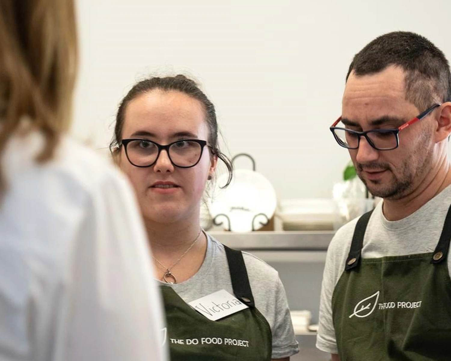 A man and a woman wearing cafe aprons serve a customer at NDIS registered disability service Distinctive Options