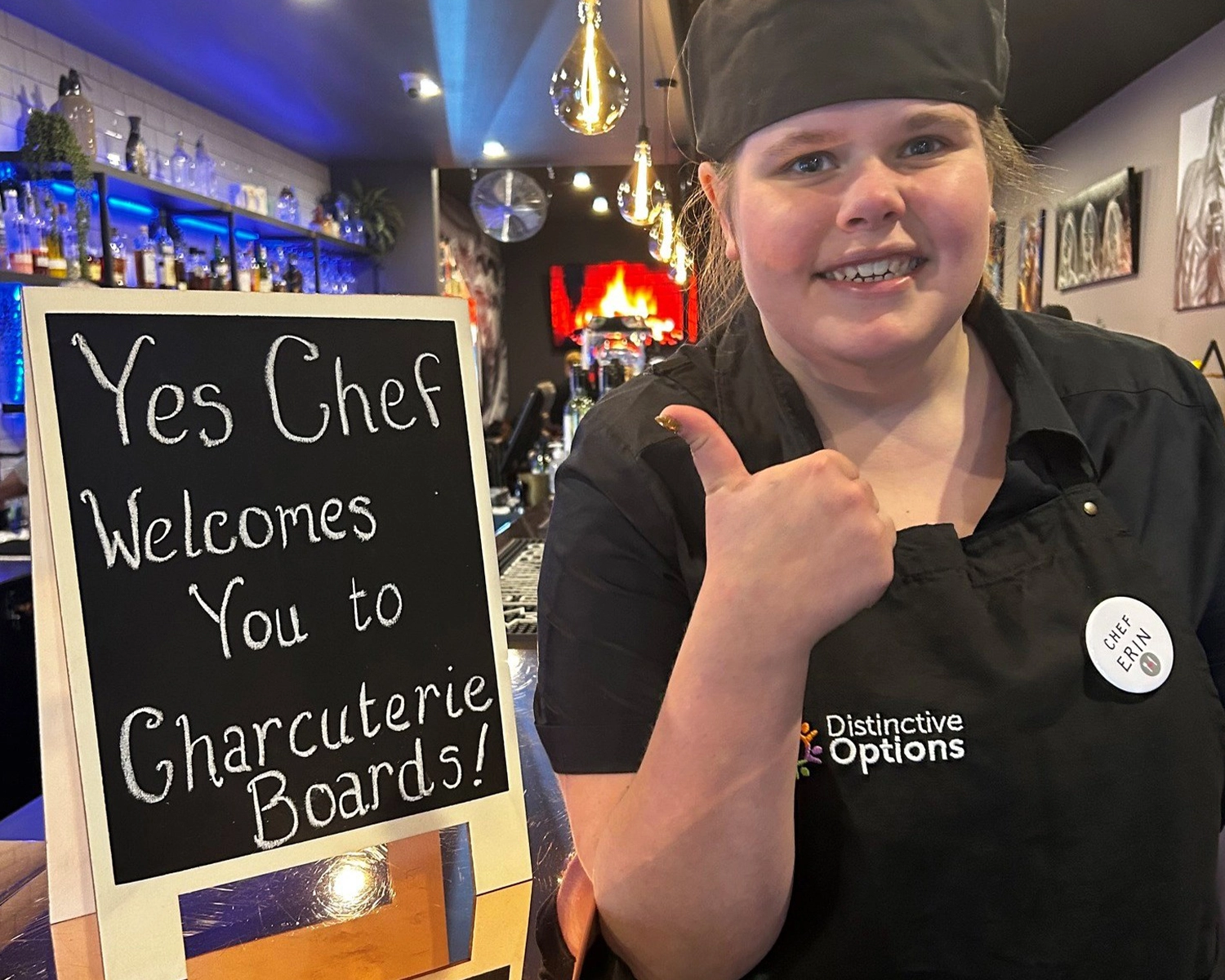 A woman wearing a cook's apron smiles while working at a cafe at NDIS registered disability service Distinctive Options