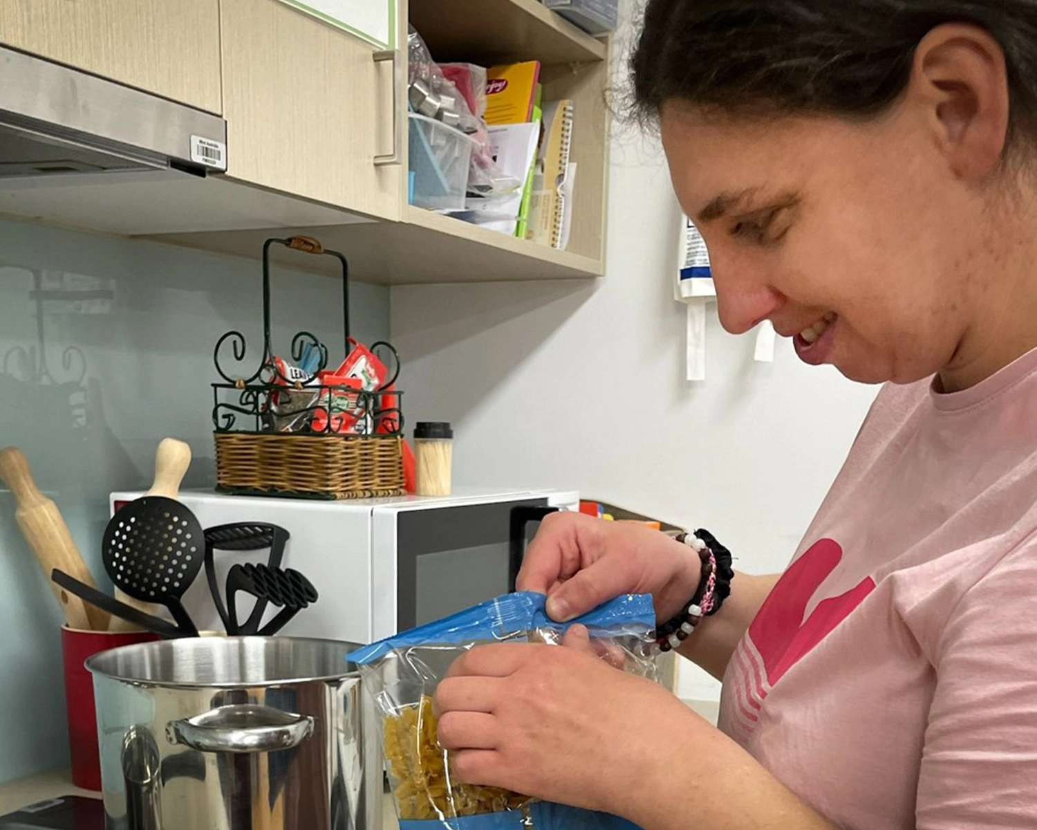 a woman opens a packet of pasta in a kitchen