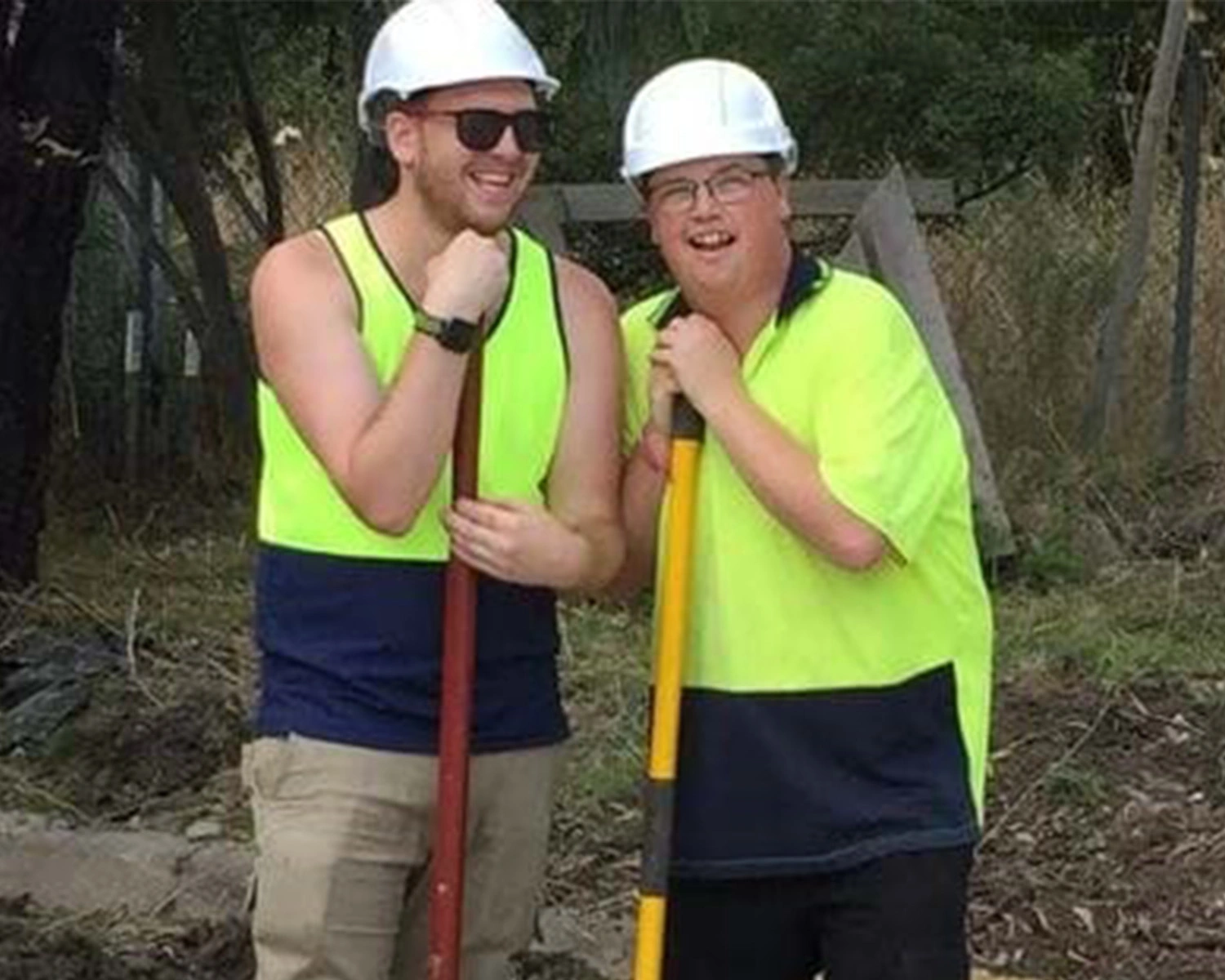 Two men lean on garden shovels while smiling at NDIS registered disability service Distinctive Options