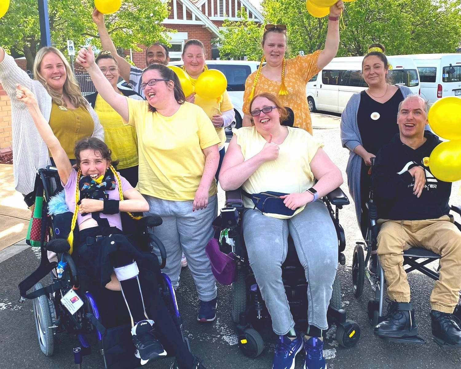 A group of people wearing yellow balloons smile at​ NDIS registered disability provider Distinctive Options