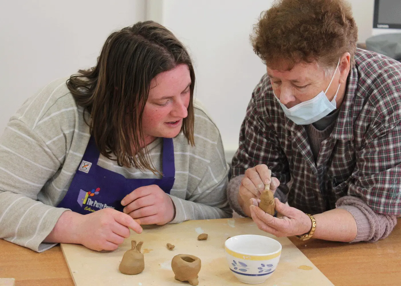 A teacher shows a student how to shape clay