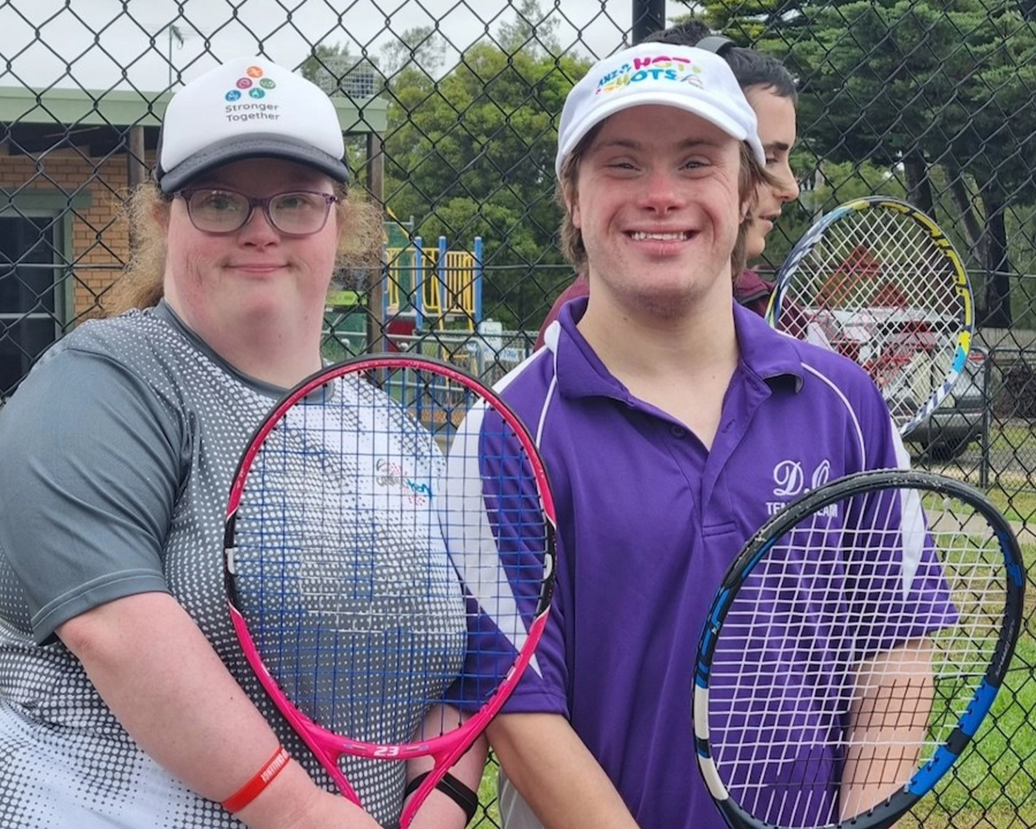 Two people stand at a tennis court holding tennis racquets at NDIS registered disability service Distinctive Options